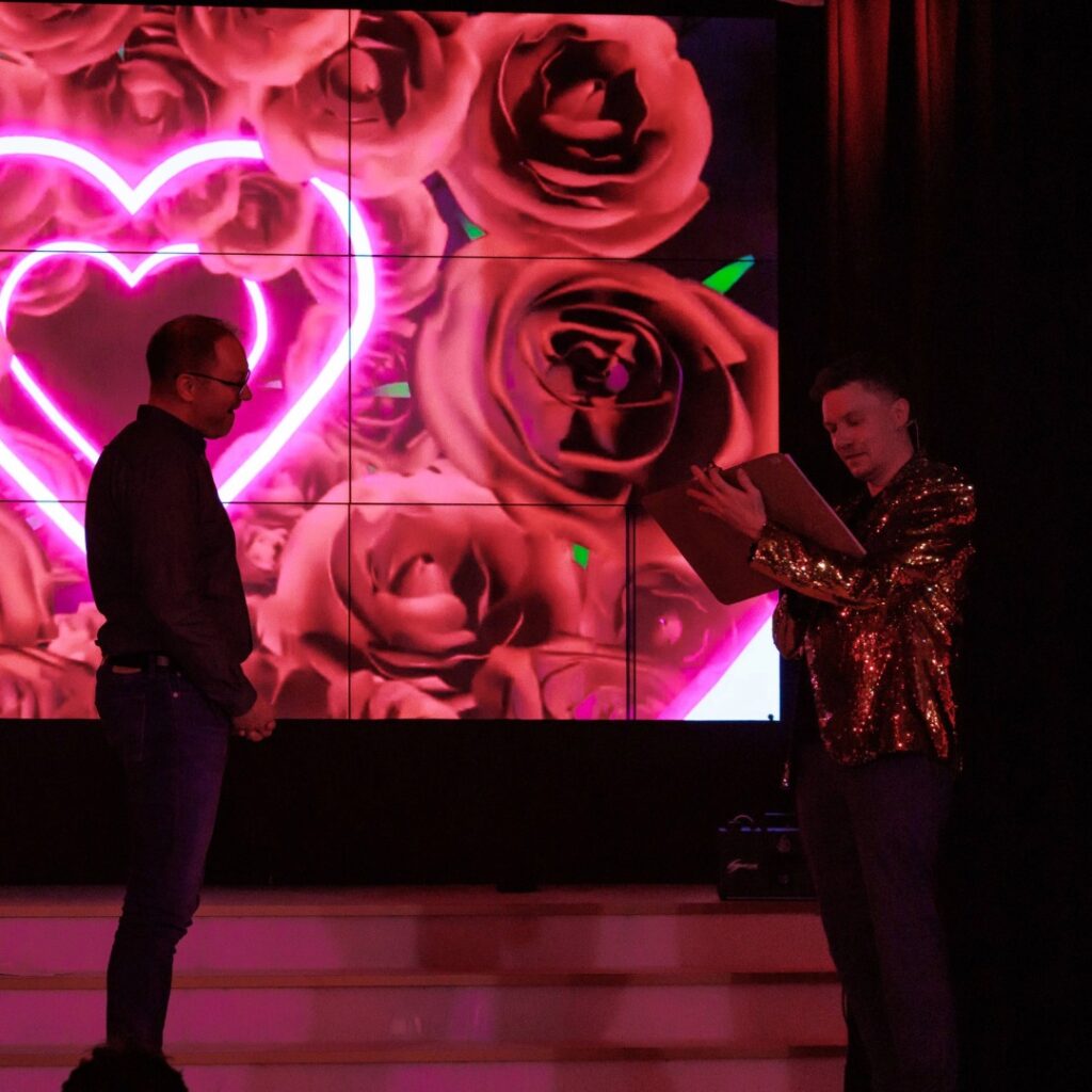 Thomas Majka interagiert mit einem Zuschauer auf der Bühne bei rotem Licht während einer Zaubershow